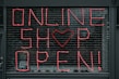 Large letters formed in pink string spell out 'ONLINE SHOP OPEN!' on a black metal grid. A heart shape replaces the letter 'O' in the word 'SHOP'. The scene seems to depict a storefront or window display.