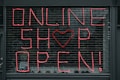 Large letters formed in pink string spell out 'ONLINE SHOP OPEN!' on a black metal grid. A heart shape replaces the letter 'O' in the word 'SHOP'. The scene seems to depict a storefront or window display.