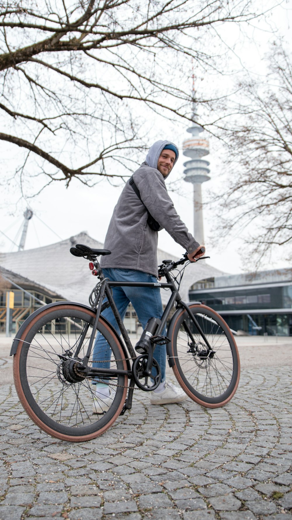 man in gray jacket and blue denim jeans riding on black bicycle during daytime