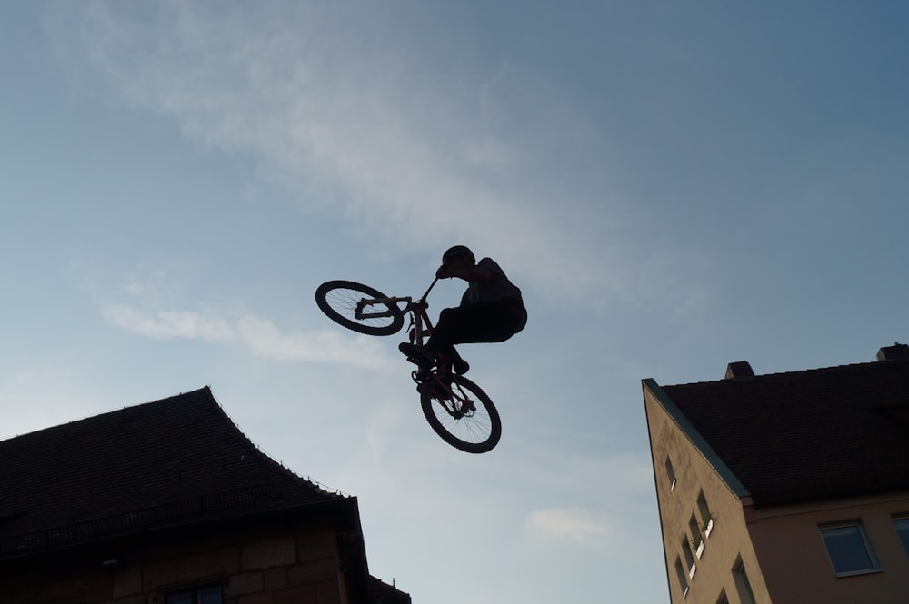 silhouette of man riding bicycle on mid air during daytime