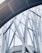 Abstract architectural structure featuring intersecting metal beams and large glass panels forming geometric patterns. The design appears modern and intricate, showcasing a blend of curves and straight lines.