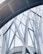 Abstract architectural structure featuring intersecting metal beams and large glass panels forming geometric patterns. The design appears modern and intricate, showcasing a blend of curves and straight lines.