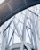 Abstract architectural structure featuring intersecting metal beams and large glass panels forming geometric patterns. The design appears modern and intricate, showcasing a blend of curves and straight lines.