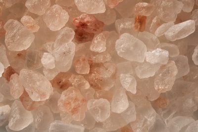 A collection of translucent, crystalline salt rocks, varying in size and displaying a mixture of light pink and white hues.