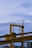 A large, industrial structure with yellow beams and railings stands under a mostly cloudy sky. A streetlight with a solar panel is fixed to the right side of the structure. There are various cables and machinery components visible around the structure.