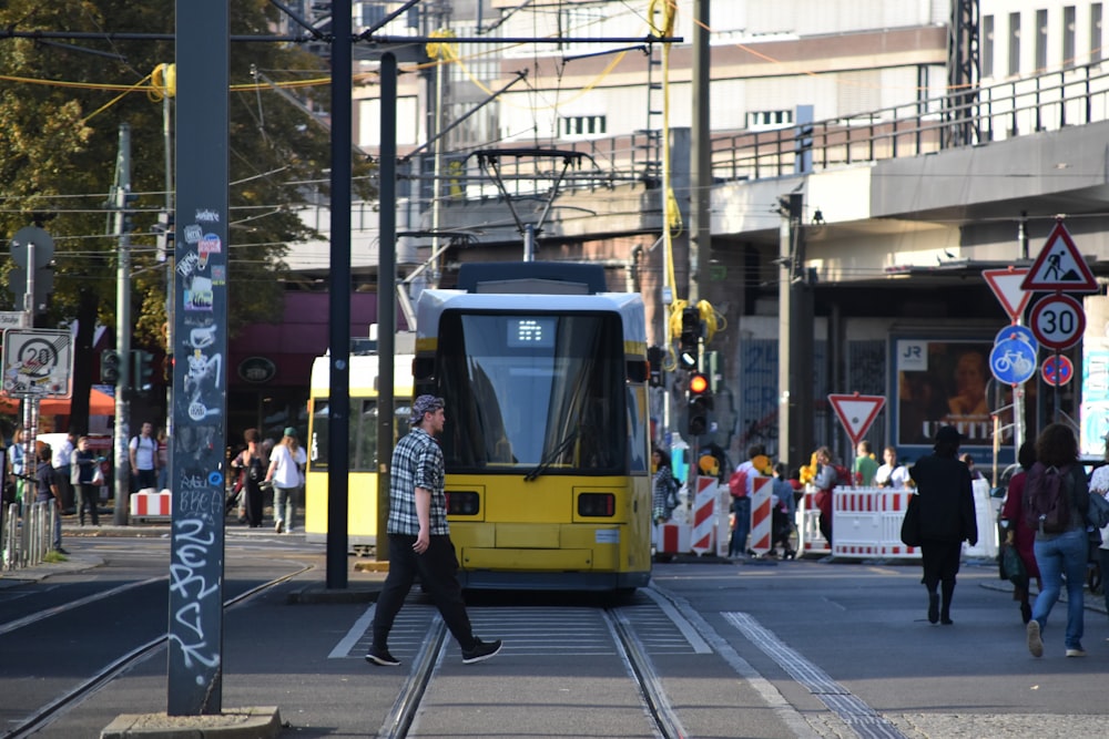 people walking on pedestrian lane near yellow and white tram during daytime