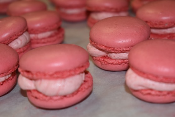 A selection of pink macarons with creamy fillings delicately arranged on a light surface. The macarons have a smooth and shiny top with the characteristic 'foot' around the bottom edge.