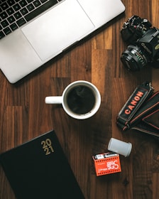 white ceramic mug beside black nikon dslr camera on brown wooden table