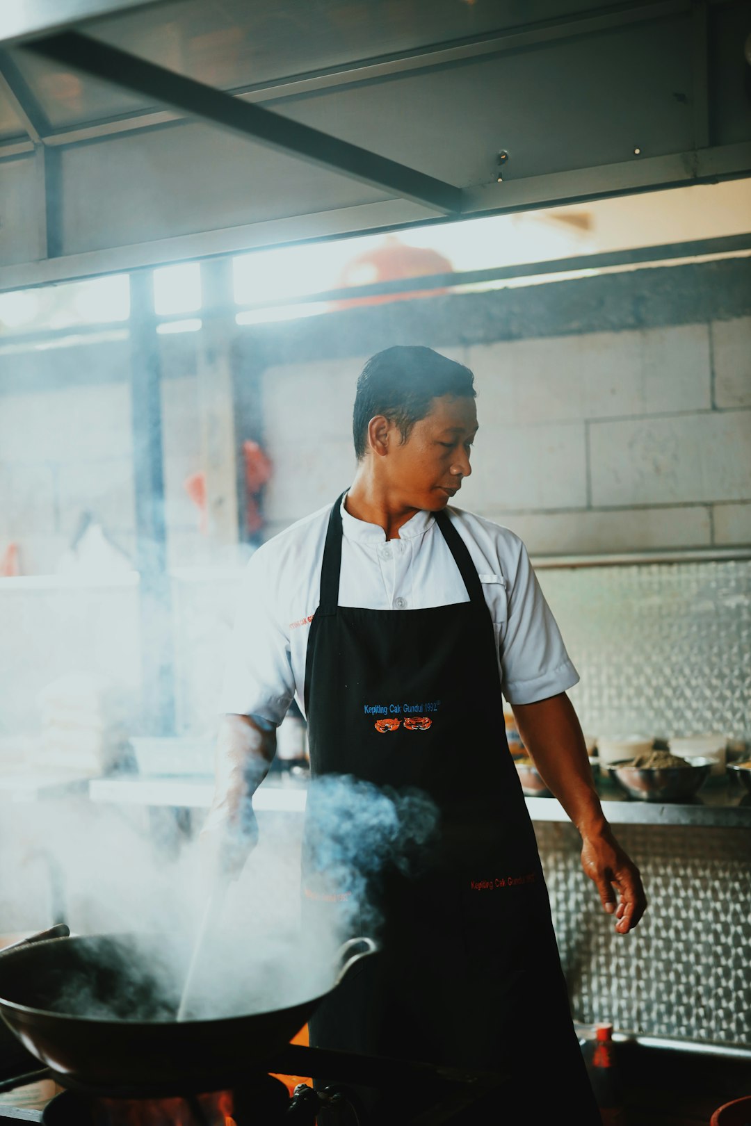 man in white apron holding black metal pan