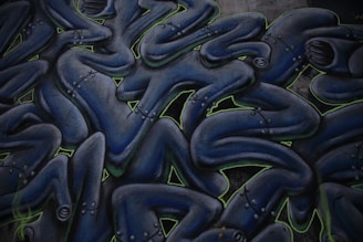 Abstract graffiti art featuring intertwined humanoid figures. The figures are dark blue with metallic, robotic details and are outlined with neon green accents. They appear to be stacked or layered in a fluid, wave-like pattern.