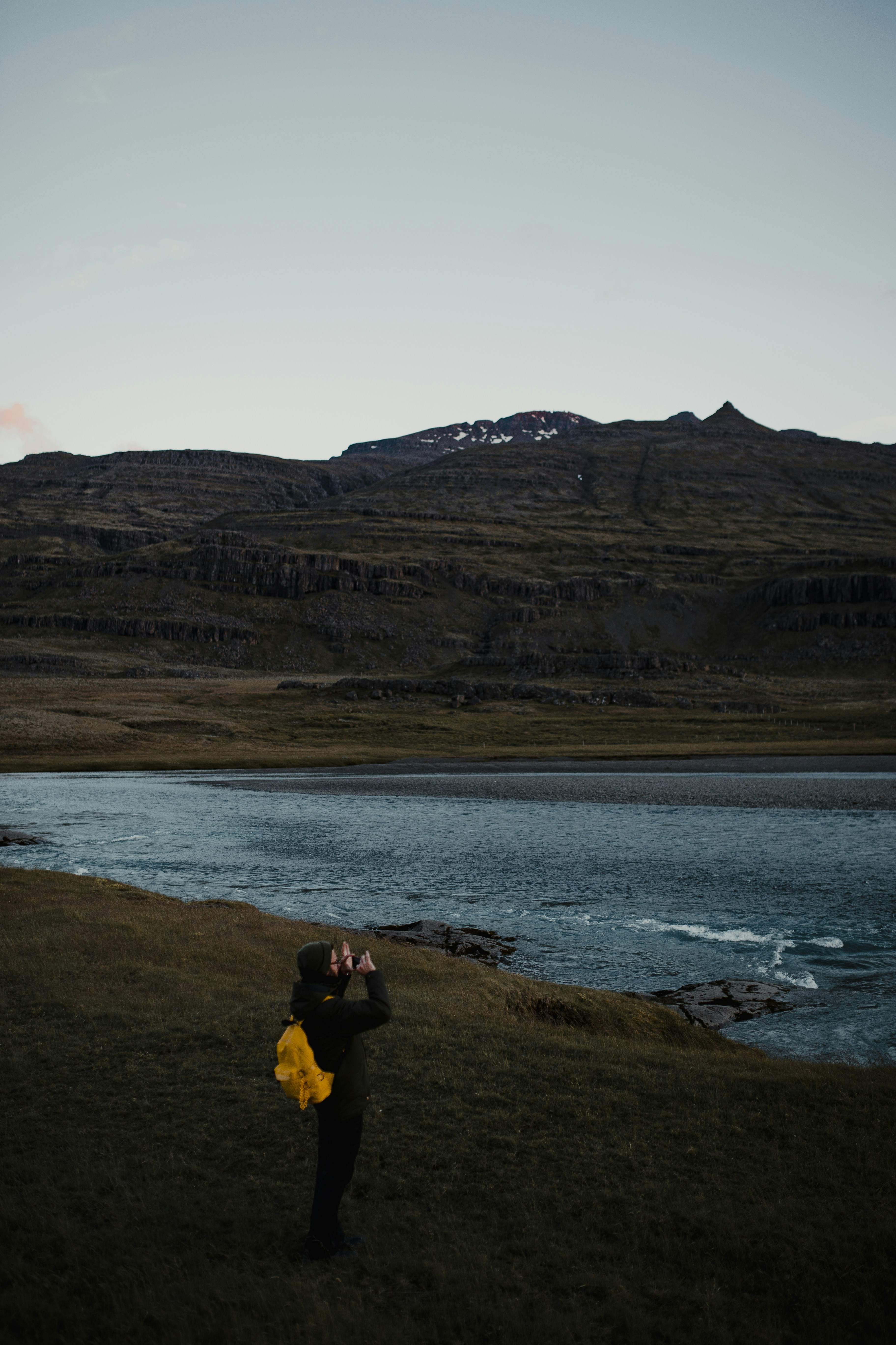 man in black jacket and yellow pants sitting on brown grass field near body of water