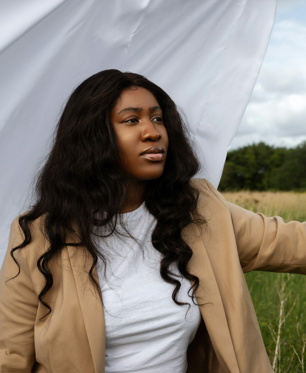 woman in white shirt and brown coat standing on green grass field during daytime