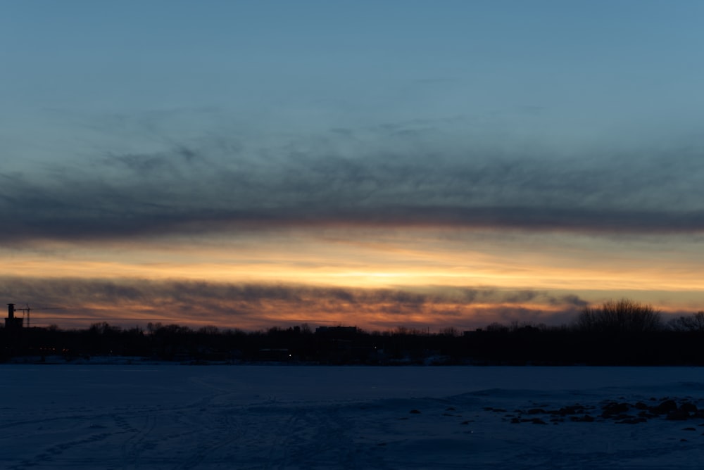 the sun is setting over a snowy field