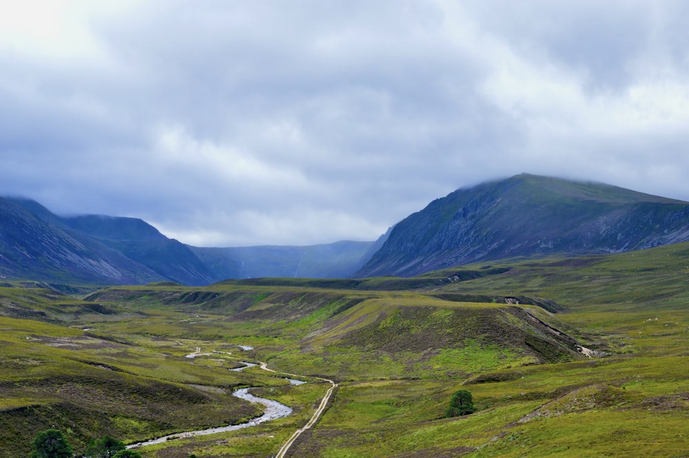 green grass field and mountain under white clouds