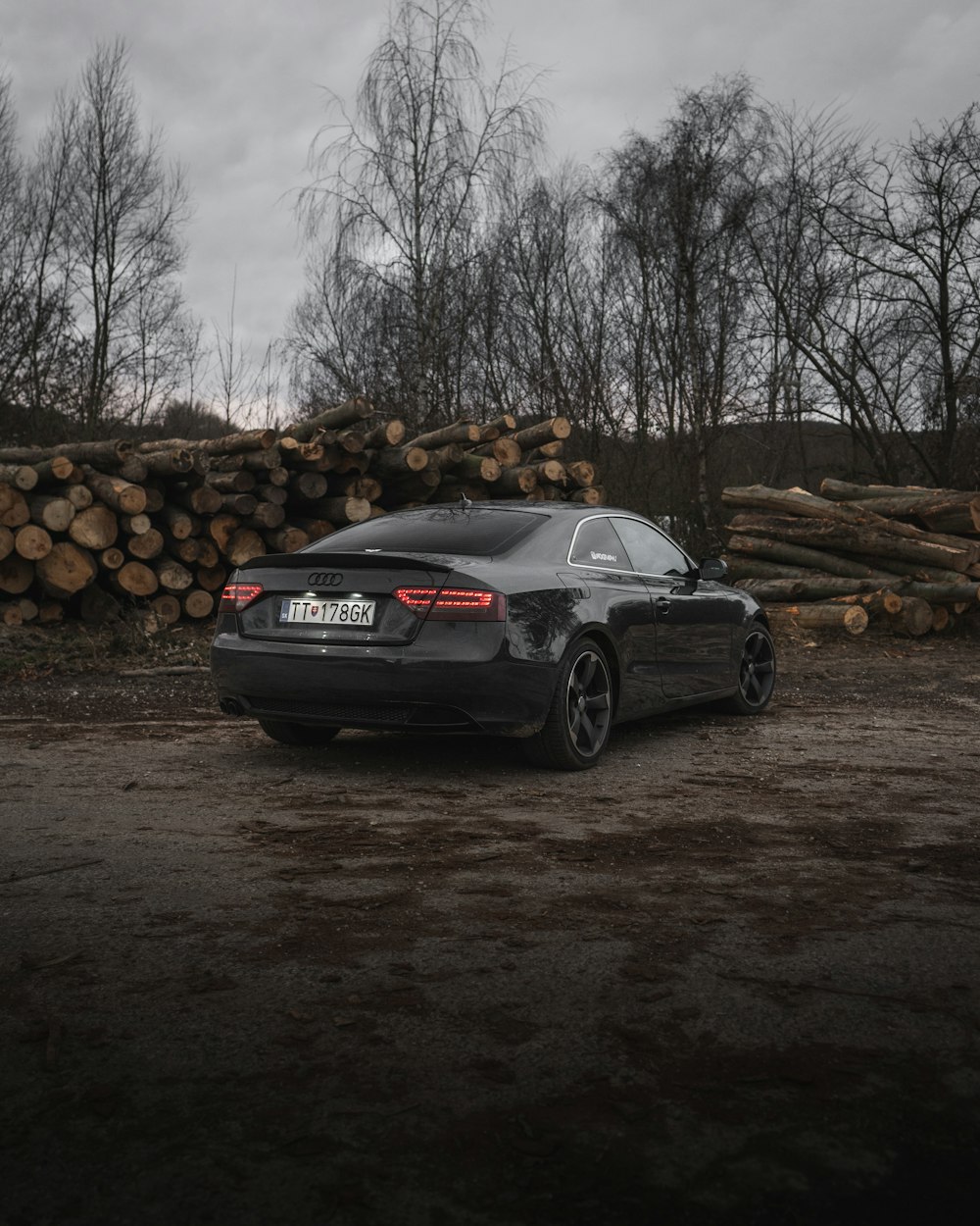 black sedan parked near pile of woods during daytime