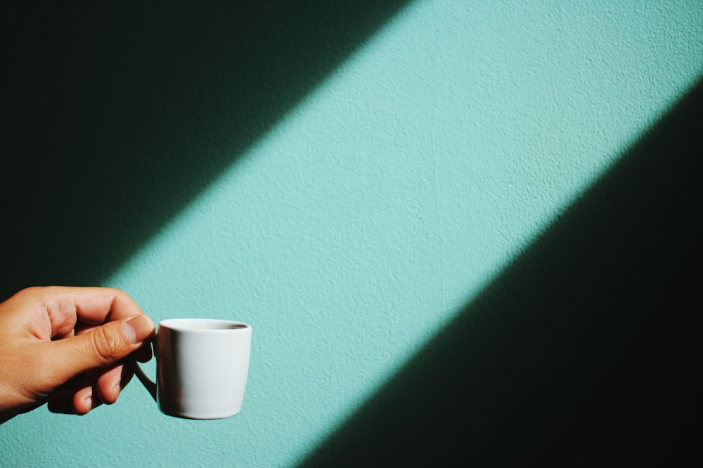 personne tenant une tasse en céramique blanche