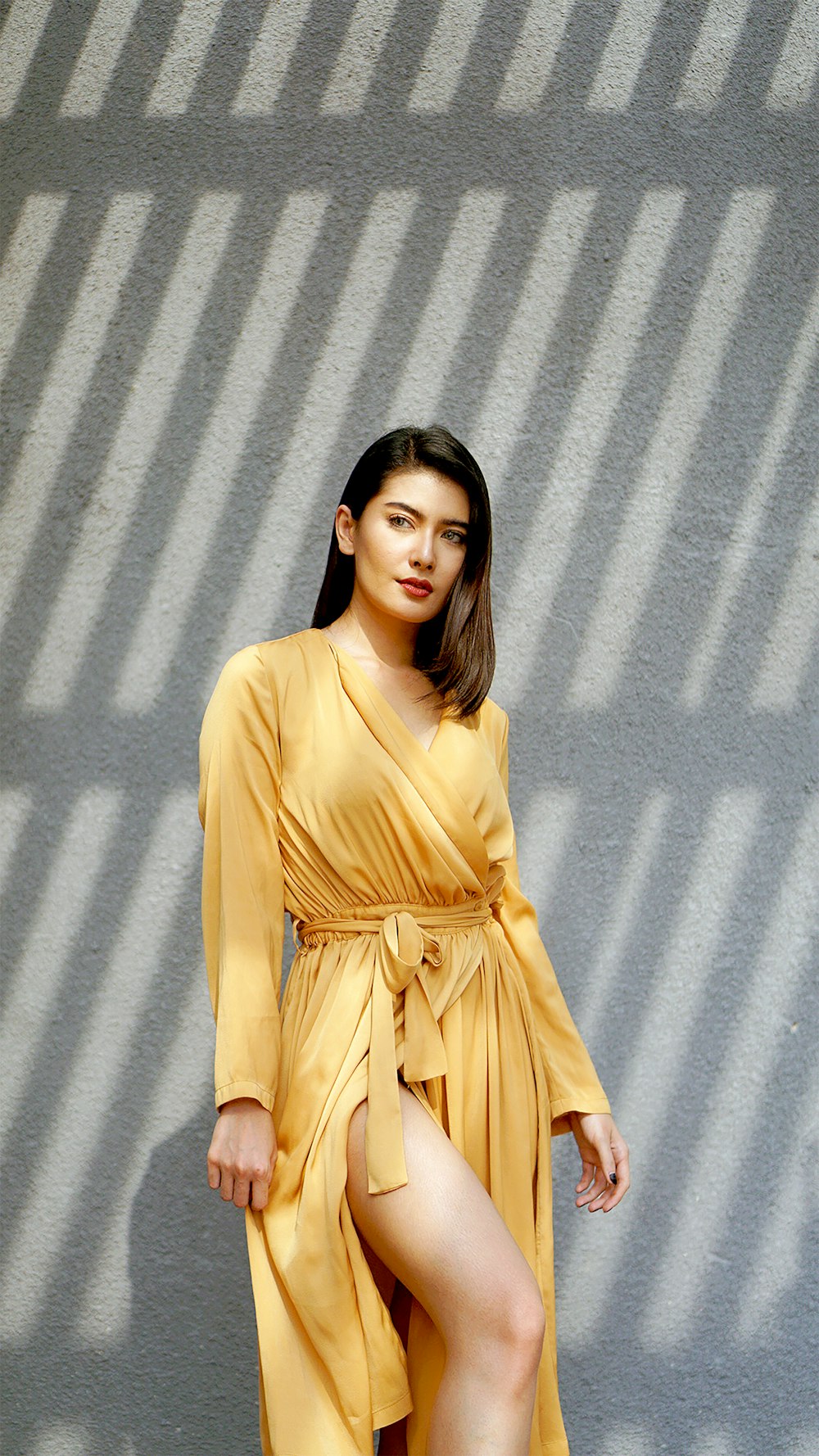 donna in abito marrone a maniche lunghe in piedi accanto al muro grigio