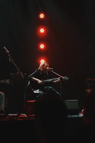 A musician strumming a guitar while seated on a wooden pew.
