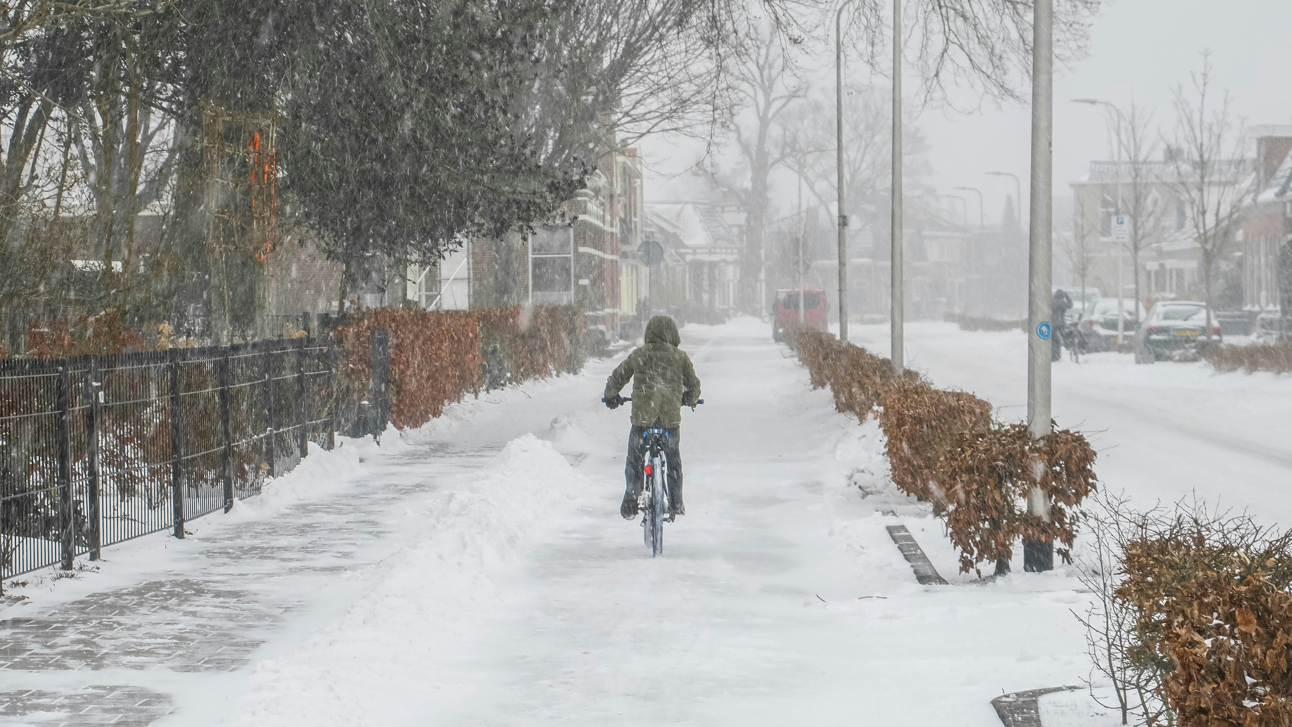 person in brown jacket riding bicycle on snow covered road during daytime