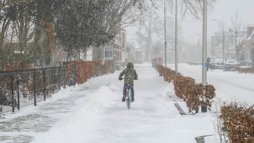 Persona en chaqueta marrón montando en bicicleta en carretera cubierta de nieve durante el día