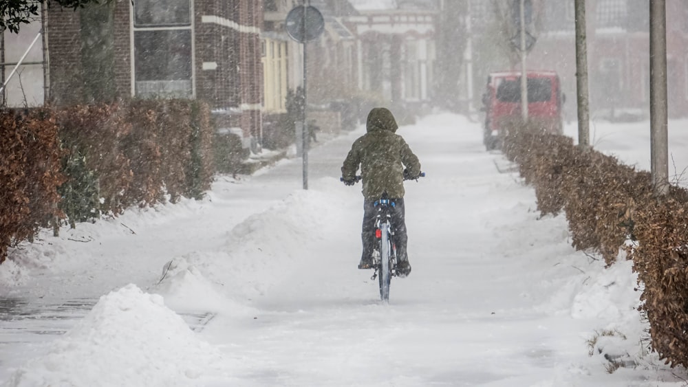 Mujer en abrigo marrón montando en bicicleta en carretera cubierta de nieve durante el día