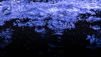 Waves of vibrant blue light ripple across a dark surface, creating a dynamic and fluid visual effect reminiscent of water or liquid textures. The intricate patterns and reflections evoke a sense of movement and energy.