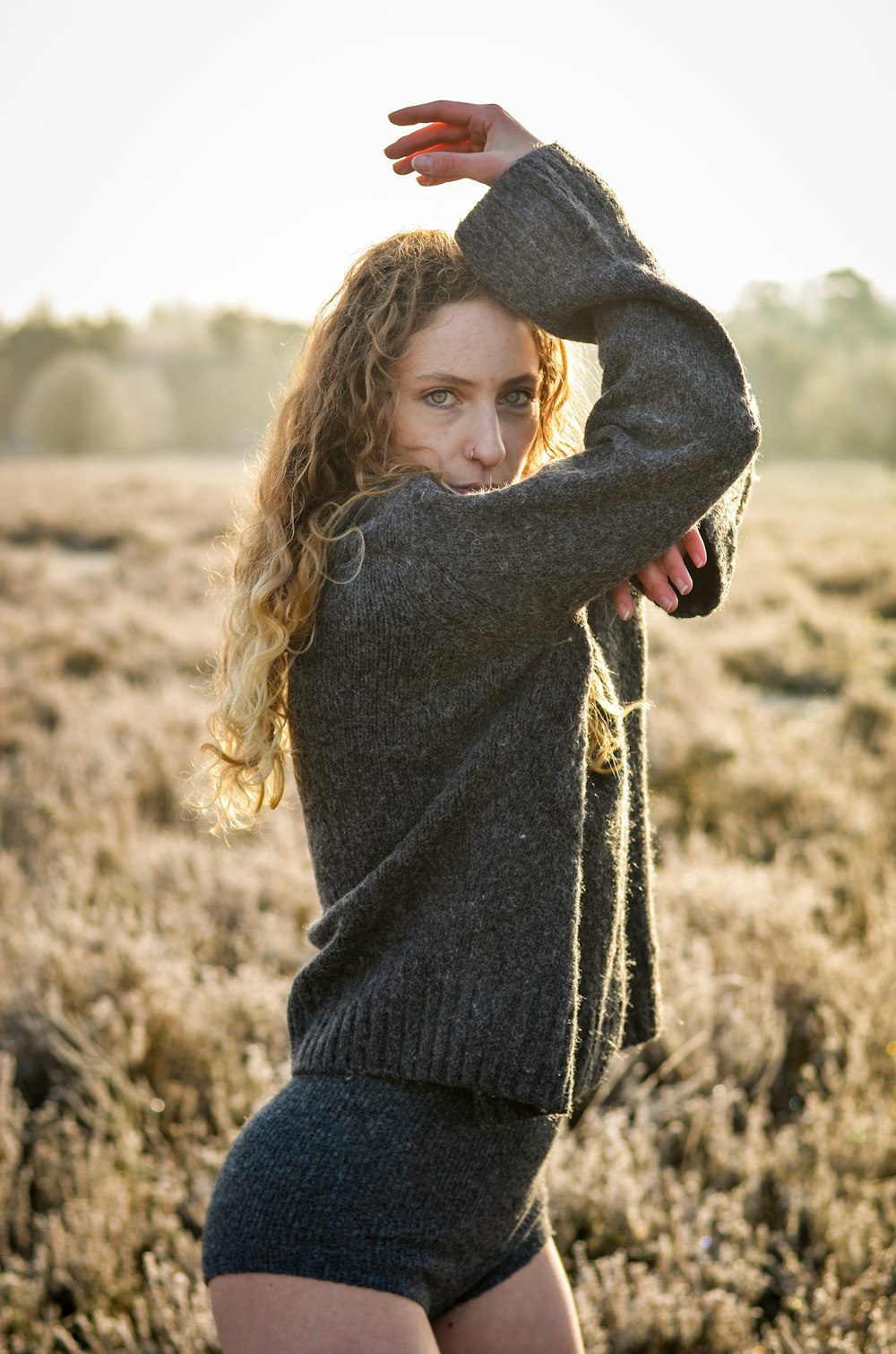 woman in black sweater and blue denim jeans standing on brown field during daytime