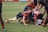 A group of rugby players engaged in a scrum on a grassy field, wearing colorful striped uniforms with matching socks. Some players are on the ground while others are bent over, actively participating in the game. The players show a mix of intense focus and physical exertion.