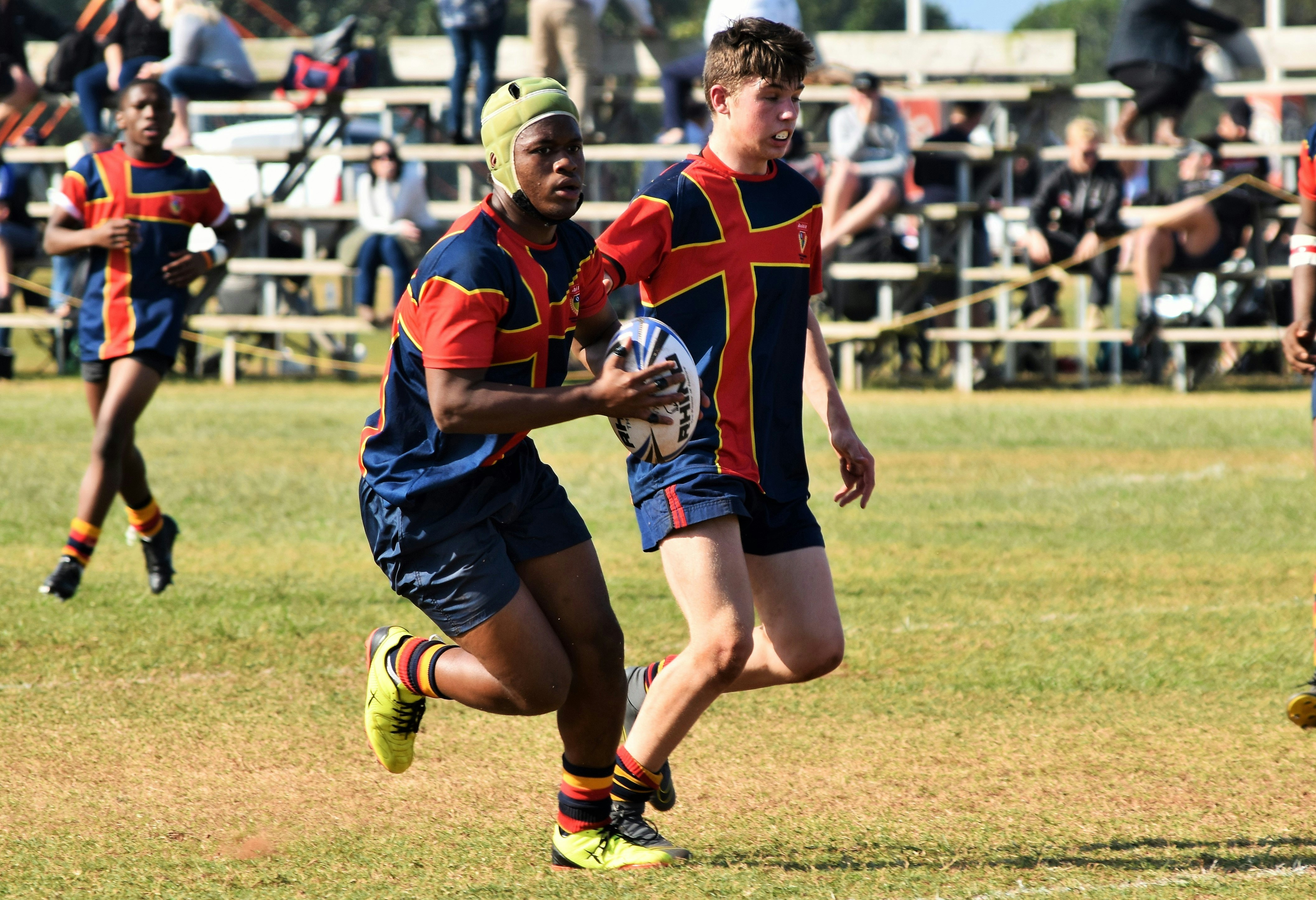 Two youngsters from the same rugby club hold the ball as they run towards the goal posts during a match.