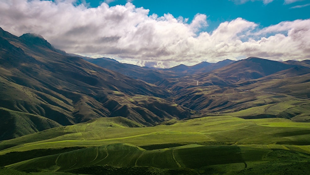 Champ d’herbe verte et montagnes sous les nuages blancs et le ciel bleu pendant la journée