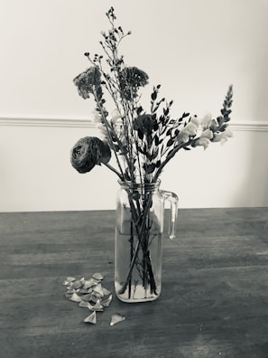 Close-up of freshly picked wildflowers in a small glass jar on a wooden table.