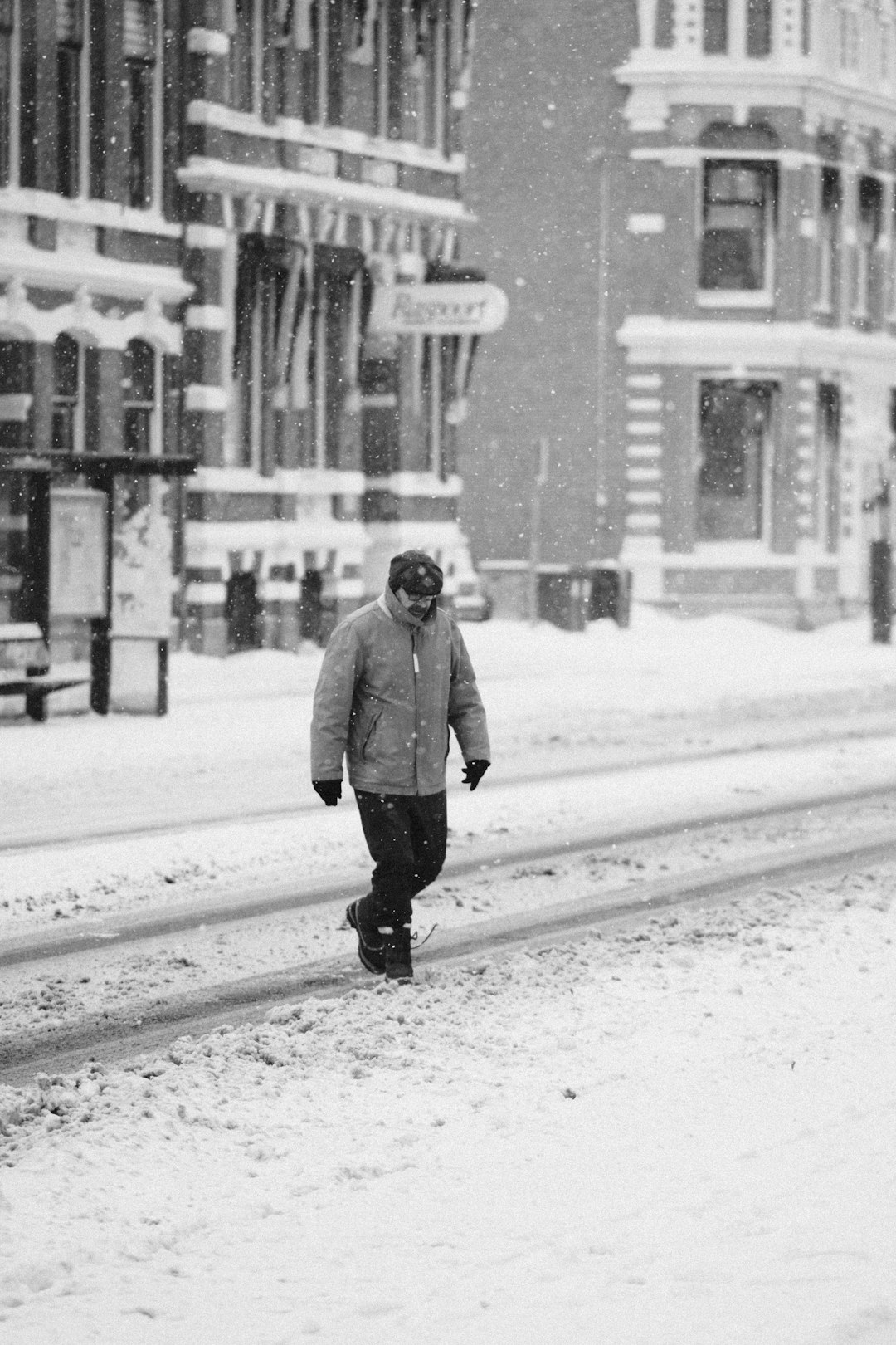 Black & white photo of bundled up man crossing a snowy street