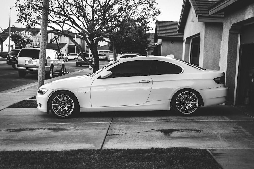 grayscale photo of coupe parked near tree