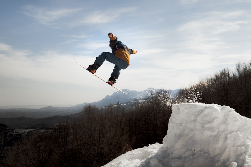 青いジャケットと黒いズボンを着た男が、昼間、雪に覆われた山でスキーブレードに乗っている