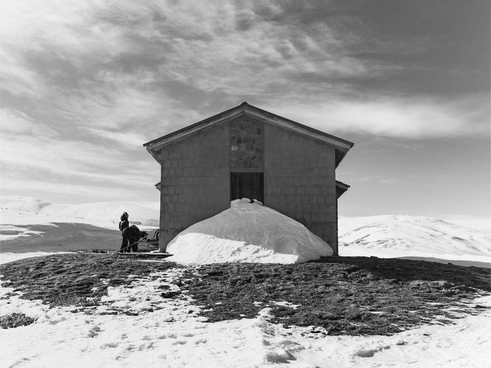 foto in scala di grigi di 2 persone sedute sulla roccia vicino all'edificio sotto il cielo nuvoloso