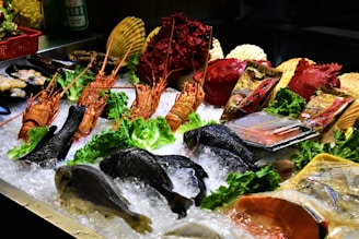 A display of fresh seafood including lobsters, fish, and shellfish is arranged on a bed of ice. Wrapped products, likely packaged seafood, are also present. The setup is enhanced with greens like lettuce for decoration, and various seafood items are placed around for an appealing presentation.
