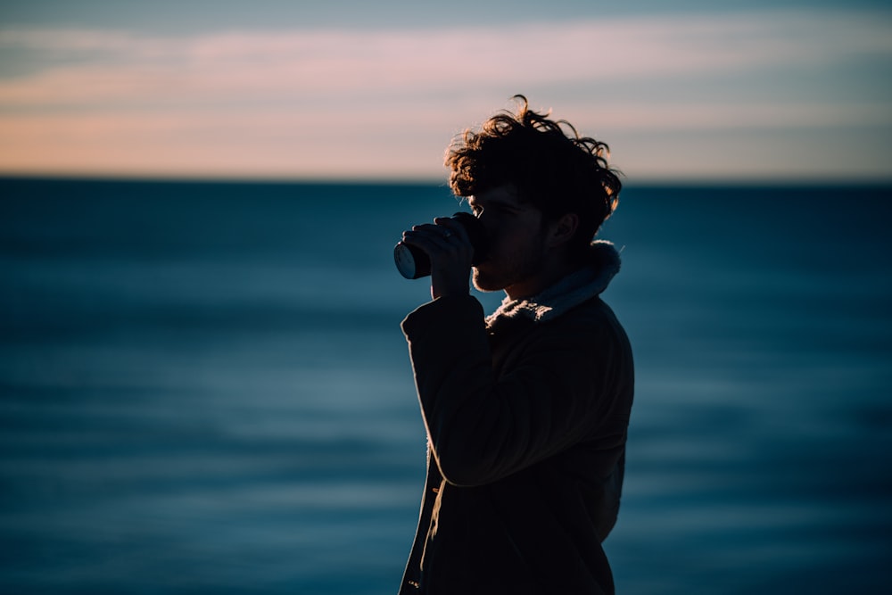 a man standing on a beach drinking from a bottle