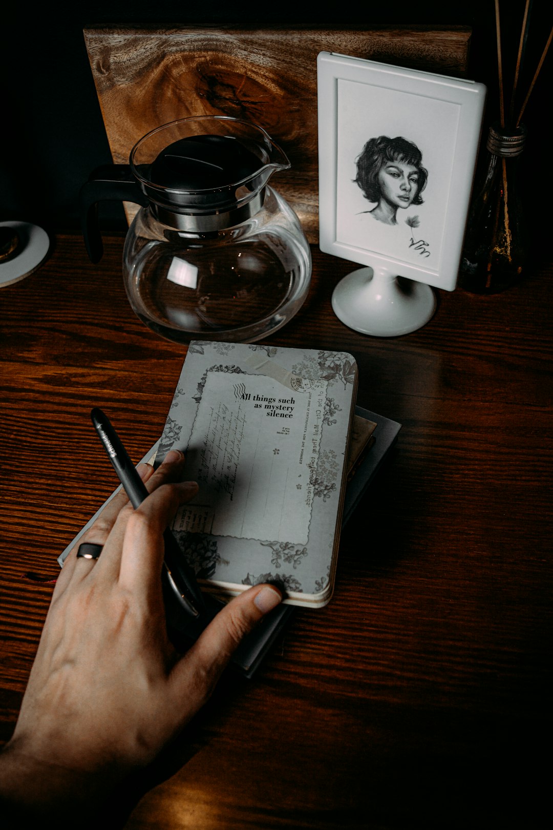 person writing on white paper beside black and silver coffee mug