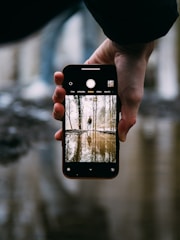A person walking while using their phone, with a smartphone screen showing a live camera feed of the path ahead.