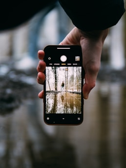 A young adult walking while looking at their smartphone, with a transparent overlay showing the view from the rear camera.