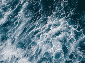 An aerial view of ocean waves creating intricate patterns with white foam on the deep blue water surface.