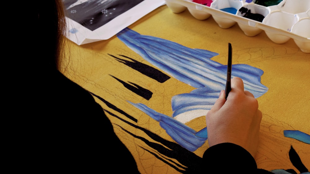 person holding black pen on blue textile