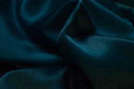 A close-up view of lustrous, dark green silk fabric with smooth textures and gentle folds creating an elegant and luxurious appearance.
