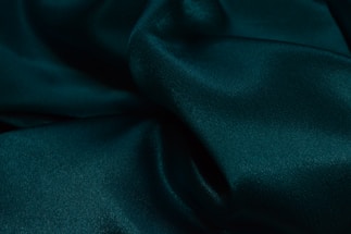 A close-up of a neatly folded deep green kameez fabric showcasing fine texture and craftsmanship.