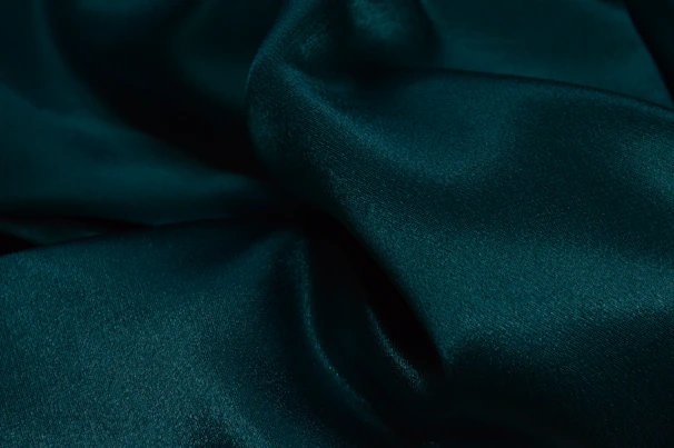 A smooth satin camisole in deep emerald green draped over a vintage chair with natural light highlighting its sheen