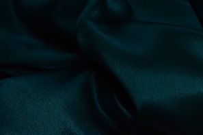 Luxurious dark green fabric with soft folds and a smooth, silky texture, creating a sense of elegance and richness.