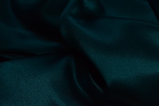Luxurious dark green fabric with soft folds and a smooth, silky texture, creating a sense of elegance and richness.