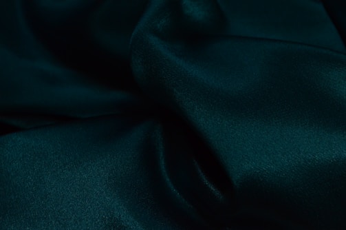 Luxurious dark green fabric with soft folds and a smooth, silky texture, creating a sense of elegance and richness.