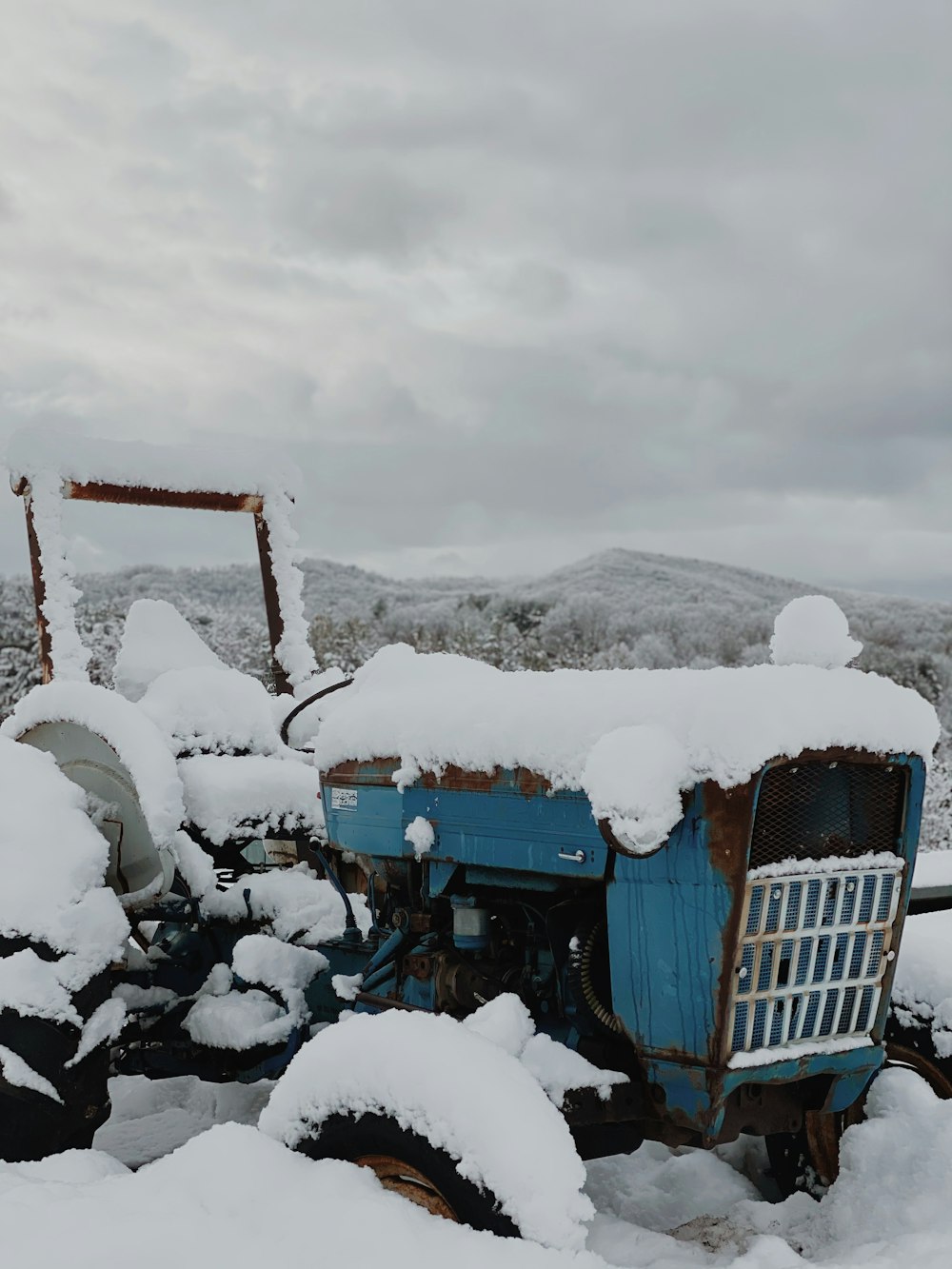 Blauer Traktor auf schneebedecktem Boden unter bewölktem Himmel