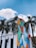 A white building featuring a large, colorful mural with abstract patterns formed by vibrant geometric shapes in red, blue, orange, green, and black tones. Several tall palm trees are positioned in front of the structure, and a bright blue sky with scattered clouds forms the background.